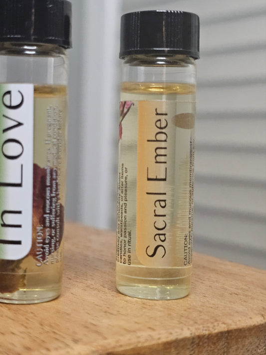 Two small bottles labeled 'In Love' and 'Sacral Ember' on a wooden surface.